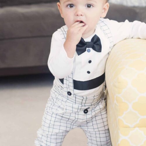Baby wearing white baptism outfit with grid pattern leggings and black bow tie