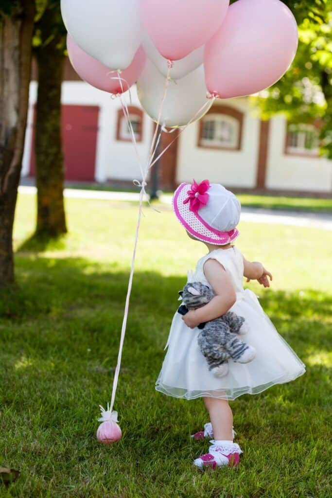 Formally dressed little girl holding stuffed animal playing with balloons outside.